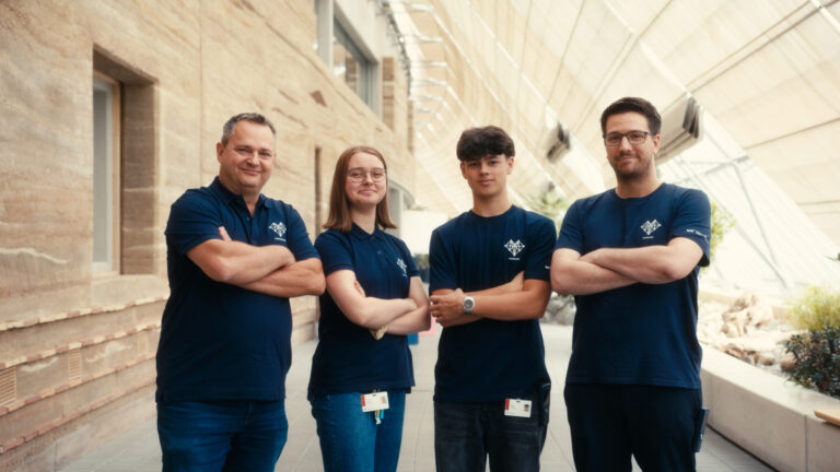 Vier IT-Teammitglieder stehen mit verschränkten Armen in einem hellen Flur.
