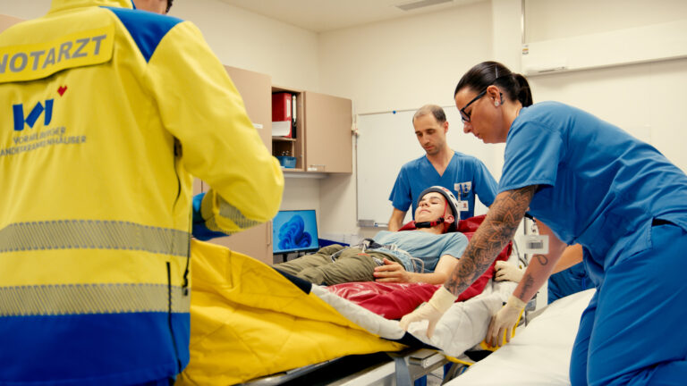Ein Notarzt und Pflegekräfte versorgen gemeinsam einen verletzten Patienten auf einer Rettungsliege.