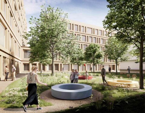 Ein parkähnlich gestalteter Innenhof mit Bäumen, Grünflächen und bunten, kreisrunden Sitzgelegenheiten vor der modernen Klinikfassade.