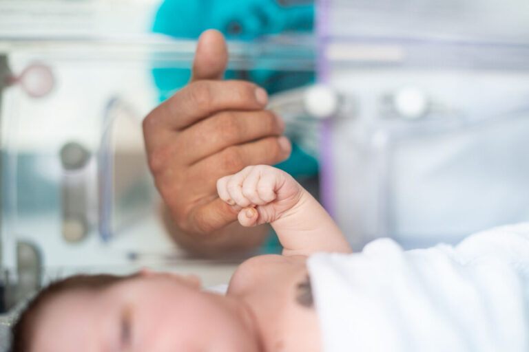 Nahaufnahme eines Neugeborenen, dessen kleine Hand den Finger eines Erwachsenen umschließt.