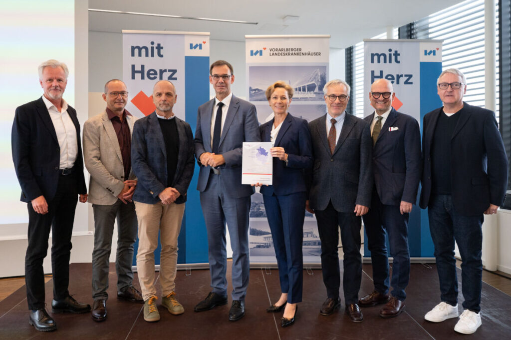 Acht Vertreterinnen und Vertreter aus Politik und Gesundheitswesen stehen nebeneinander vor Informationsbannern und halten gemeinsam ein Dokument in die Kamera.
