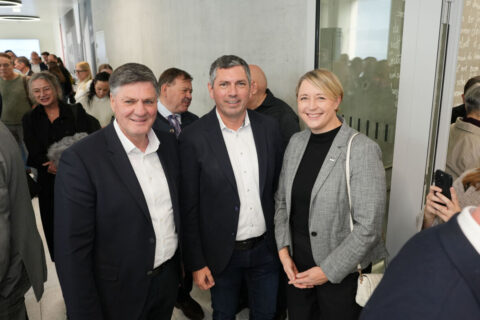 Drei Personen lächeln während der Eröffnungsfeier gemeinsam in die Kamera.