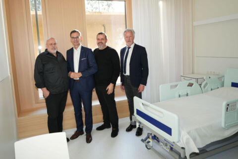 Landeshauptmann Mag. Markus Wallner, Geschäftsführer VLKH Dir. Dr. Gerald Fleisch, Geschäftsführung von Marte.Marte Architekten ZT Bernhard und Stefan Marte stehen lächelnd in einem neu eingerichteten Patientenzimmer neben einem Krankenhausbett.