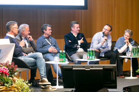 Sechs Expertinnen und Experten sitzen während einer Podiumsdiskussion auf der Bühne und tauschen sich mit Mikrofonen aus.