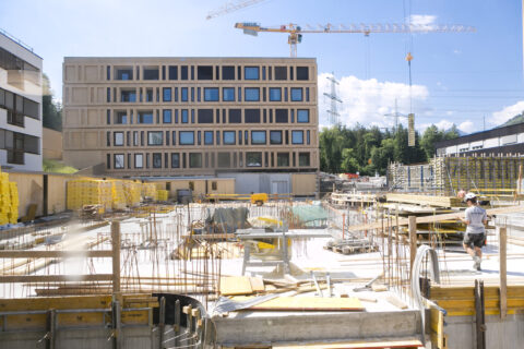 Baustelle des Neubaus der Kinder- und Jugendpsychiatrie mit Baukränen, Betonfundamenten und Bauarbeitern im Vordergrund vor einem modernen Klinikgebäude.