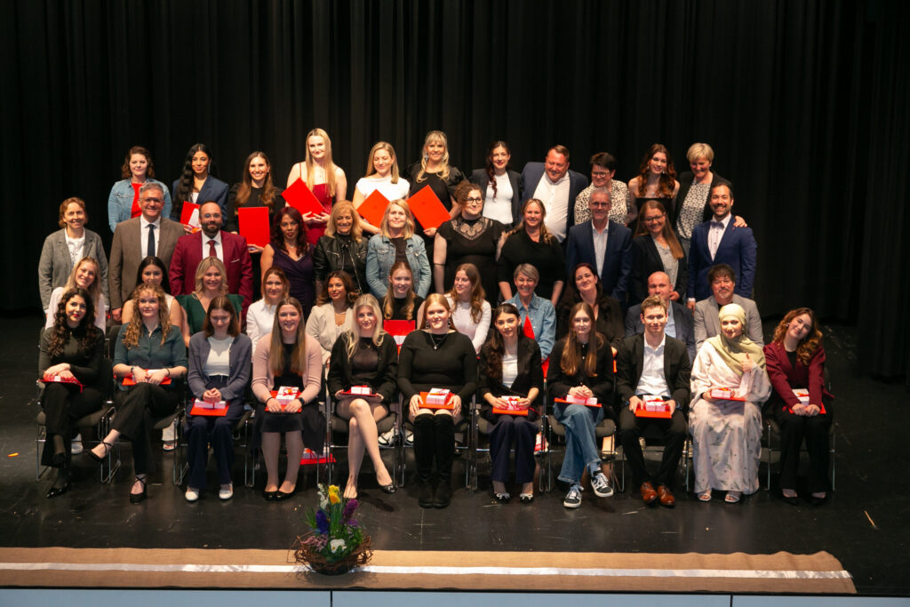 Festliches Gruppenfoto der Absolventen der Pflegeassistenz, Pflegefachassistenz und Fachsozialbetreuung auf der Bühne während der Feierstunde am Lernort Feldkirch