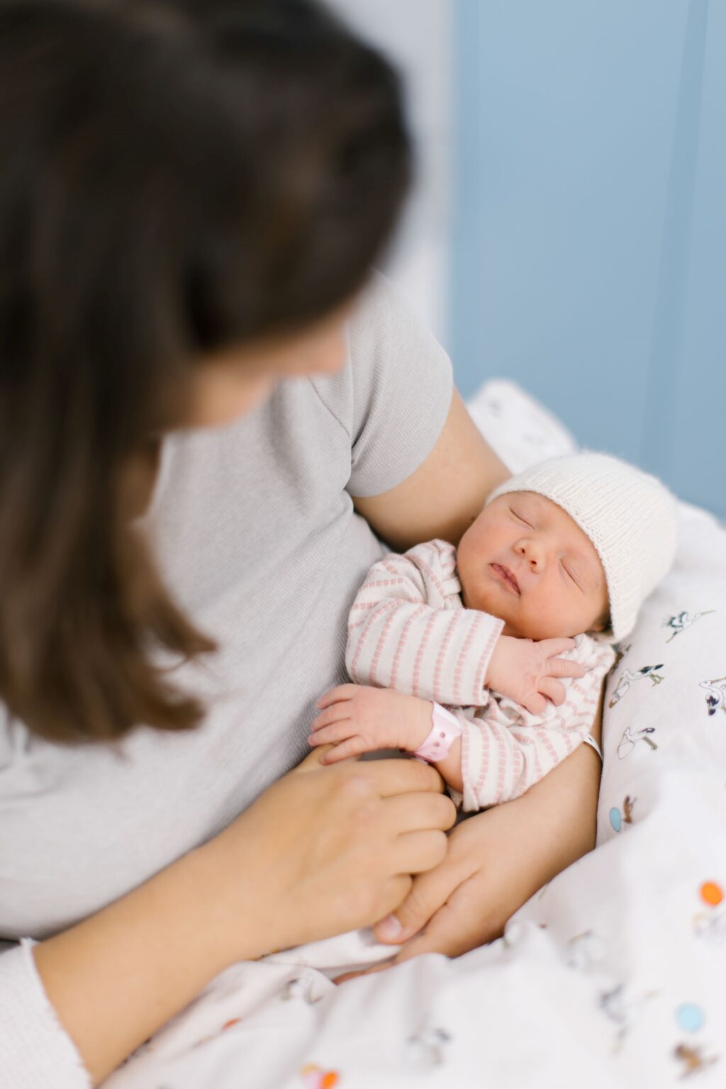 Eine Mutter hält ihr schlafendes Neugeborenes mit weißer Strickmütze behutsam im Arm.