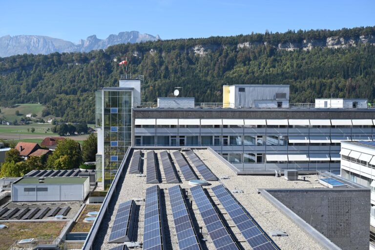 Aufgeständerte Photovoltaikmodule auf dem Dach des Landeskrankenhauses Feldkirch zur Nutzung erneuerbarer Energien vor der Vorarlberger Bergkulisse.